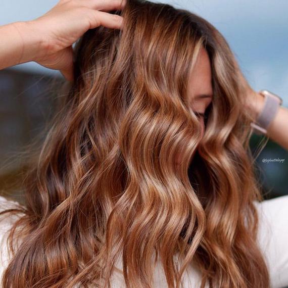 Foto einer Frau mit langem, gewelltem, hellbraunem Haar, das karamellfarbene und blonde Highlights enthält. Die Farbe wurde mit Wella Professionals