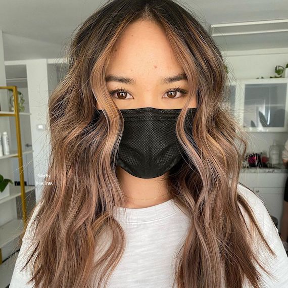 Headshot of a person with long, wavy light chocolate brown hair wearing a black mask