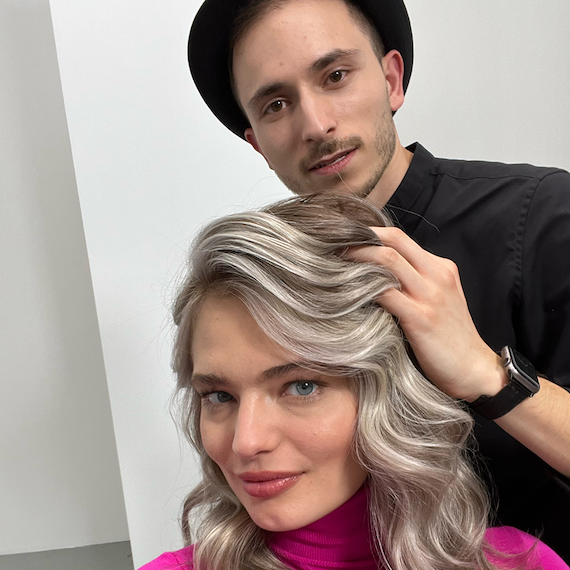 Model’s ash blonde, wavy hair is being styled by a professional hairdresser.