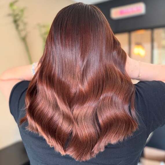 Back of model’s hair with long, glossy waves in a dark copper color.