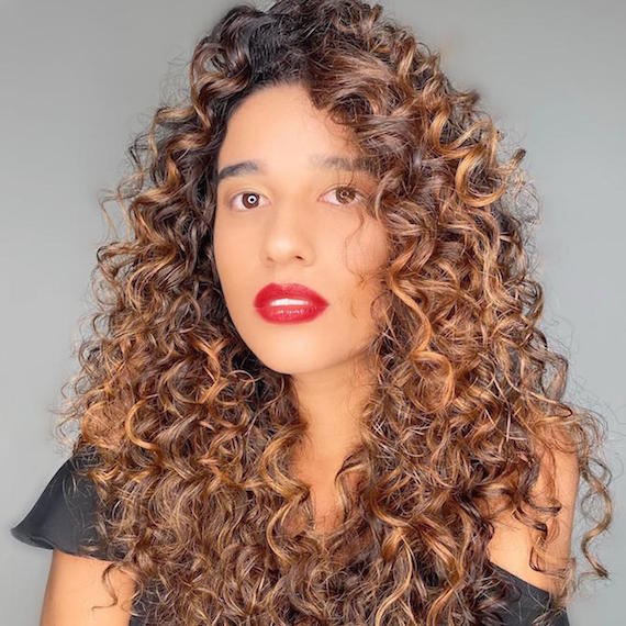 Woman wearing red lipstick with long, brown, curly hair, cared for by Wella Professionals.