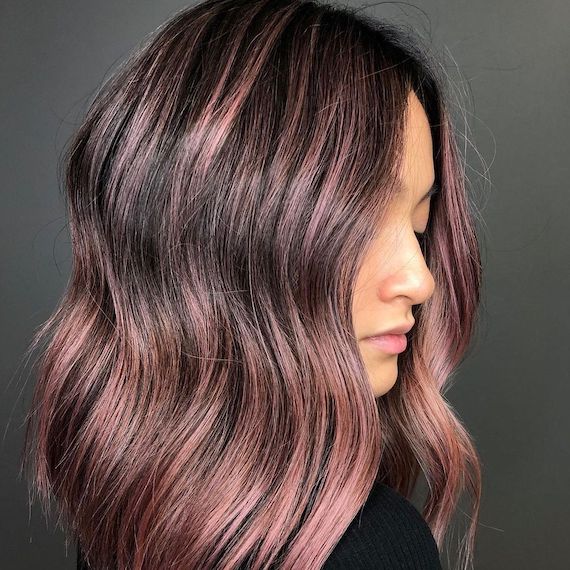Model looks to the side showing her dark brown hair featuring dusky pink highlights.