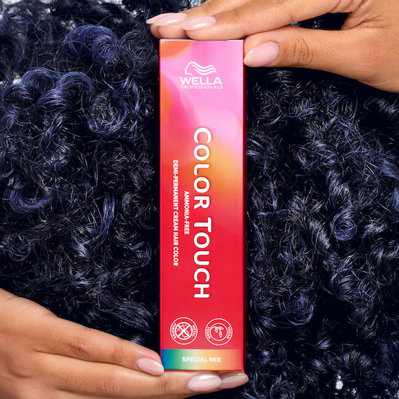 Model with dark blue, curly hair holds up a box of Color Touch.