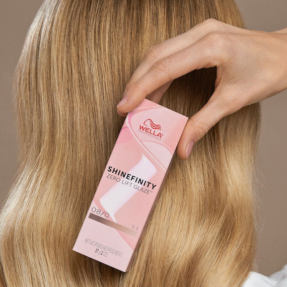 Model with honey blonde hair holds a box of SHINEFINITY.