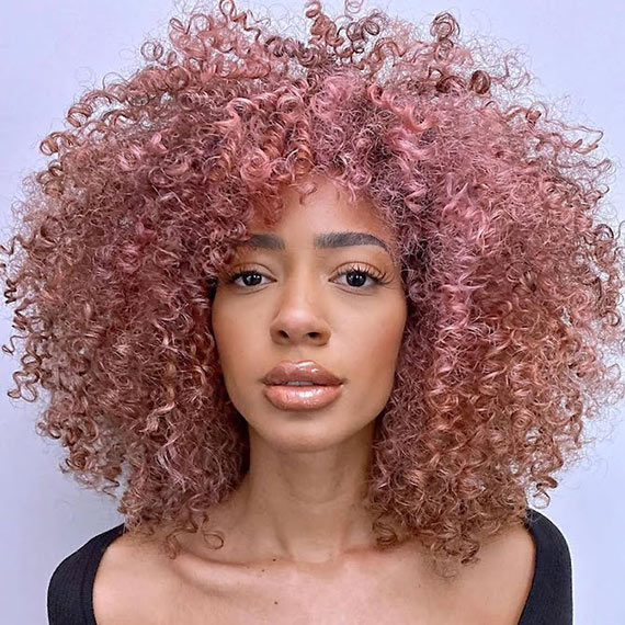 Model with a full head of dusty pink highlights through curly hair.