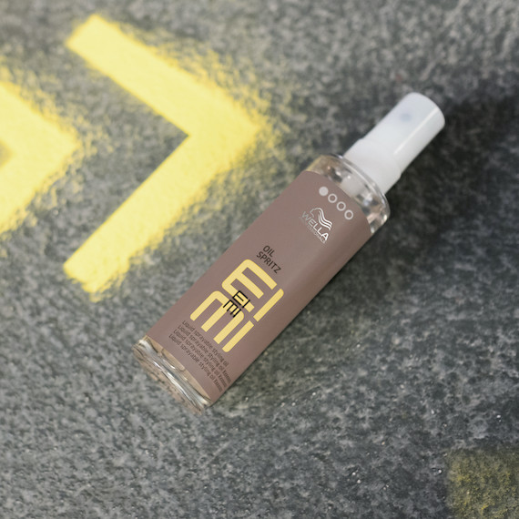EIMI Oil Spritz bottle lies flat on a concrete surface.