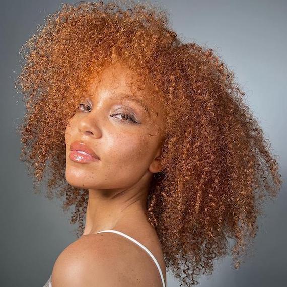 Headshot of a model with curly ginger brown hair stood in front of a grey backdrop