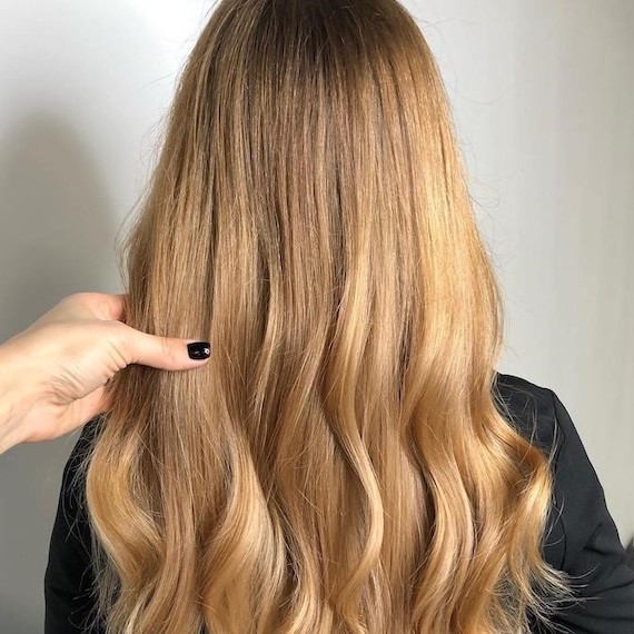 Hinterkopf einer Frau mit langem, gewelltem, rein goldblondem Haar, kreiert mit Wella Professionals.