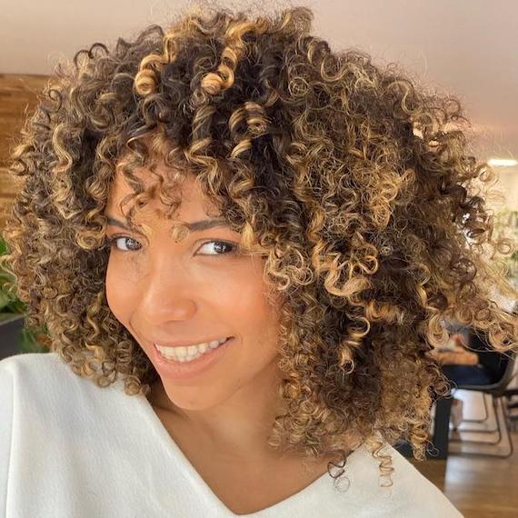 Model with dark brown, curly hair featuring golden blonde balayage.