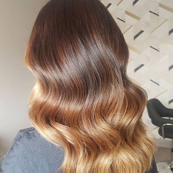 Model with long, brown hair featuring a golden blonde ombre through glossy waves.