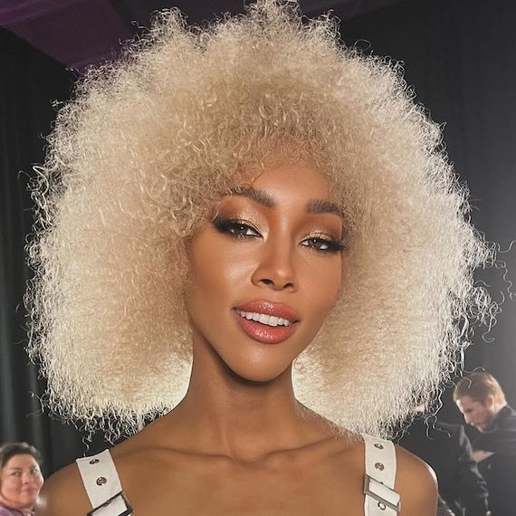 Model with radiant, tight curls in a golden platinum blonde shade.