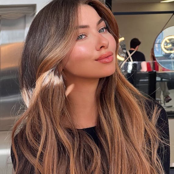 Model with long, wavy, light brown hair featuring golden balayage.