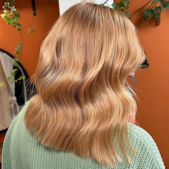 Model with glowy golden blonde hair, styled in a loose, polished wave.