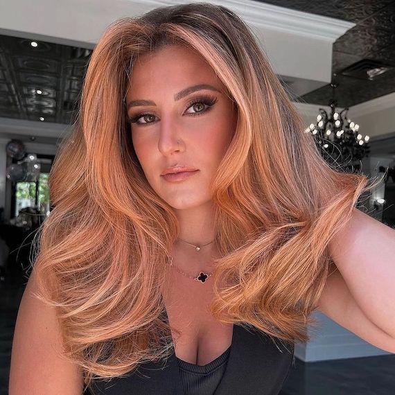 Model with long hair featuring a peachy blonde balayage, styled smooth and glossy.