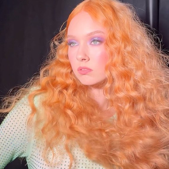 Model with ultra-long, bright strawberry blonde mermaid waves.