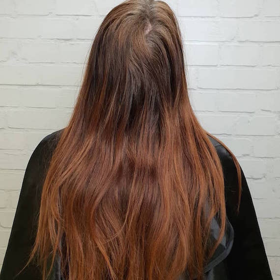 Back of woman’s head with long red-brown hair and gray roots.
