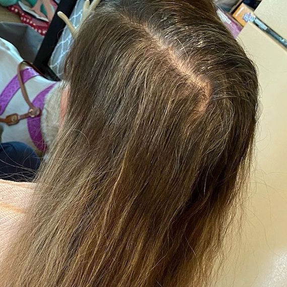 Back of woman’s head with long red-brown hair and gray roots.