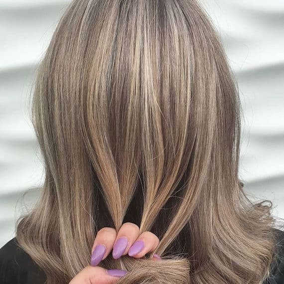 Hinterkopf einer Frau mit blondem, gewelltem Haar und Strähnen, kreiert mit Wella Professionals.