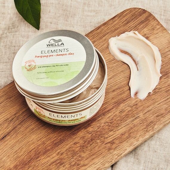 Ein Tiegel mit der Elements Pre-Shampoo Clay Mask von Wella Professionals auf einem Holzbrett
