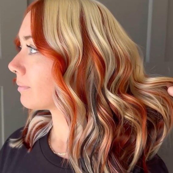 Side profile of model with wavy, blonde hair featuring pops of red and black.