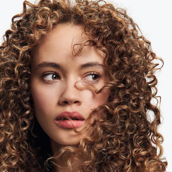 Ein Model mit lockigem, braunem Haar blickt in die Kamera.