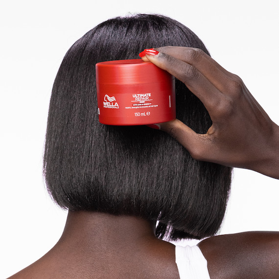 Back of model’s head with short, glossy, black hair. They’re holding up the ULTIMATE REPAIR Mask.