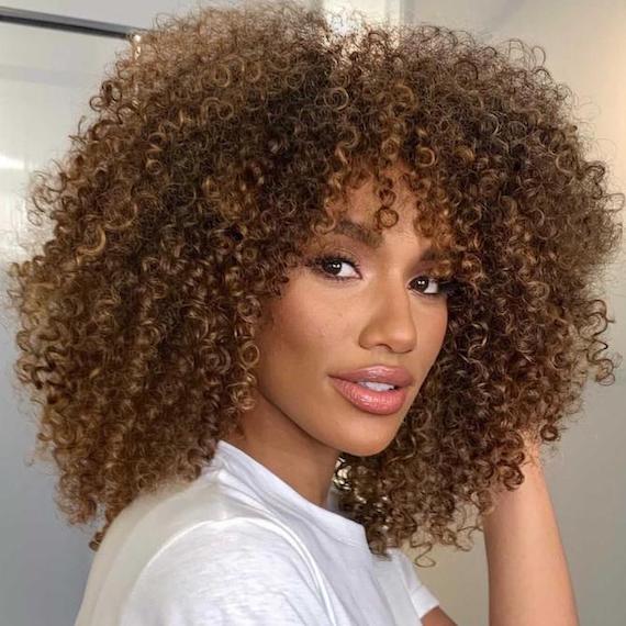 Woman smiling as she faces the camera with shiny, curly, dark brown hair.