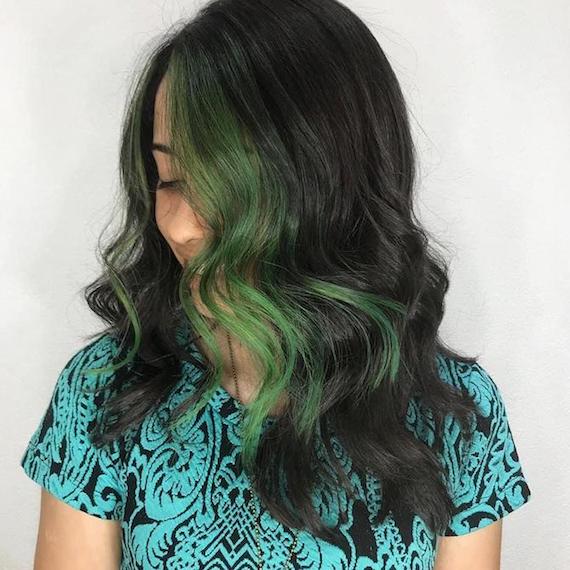 Woman with long, wavy, dark brunette hair featuring green streaks, created using Wella Professionals.