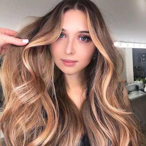 Model with long bronde hair and golden halo highlights faces camera.