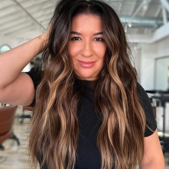 Model with long, brown, wavy hair featuring caramel highlights.