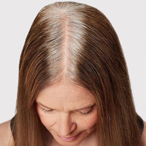Close-up of model’s white and gray roots against light brown hair.
