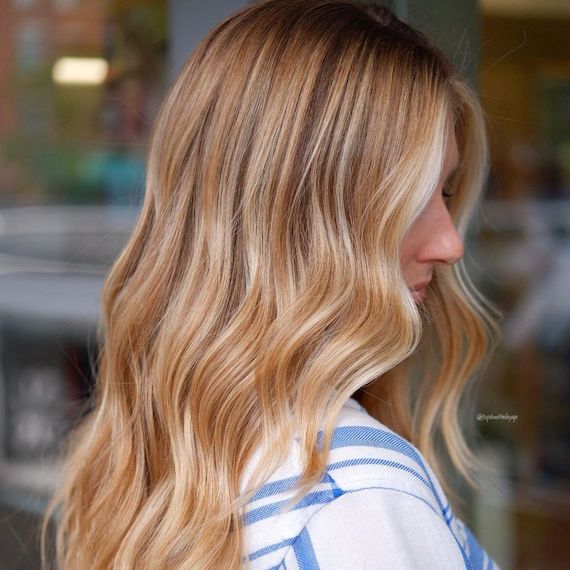 Profile of a person with long blonde hair coloured with honey highlights and a dark root shadow.