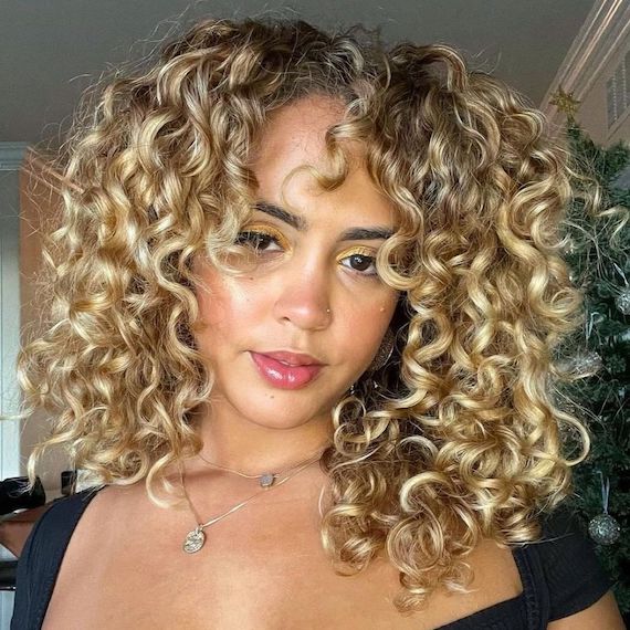Model with honey blonde, curly hair looks into the camera.