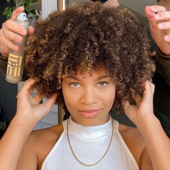Hairdresser sprays EIMI Glam Mist into model’s curly, brown hair.