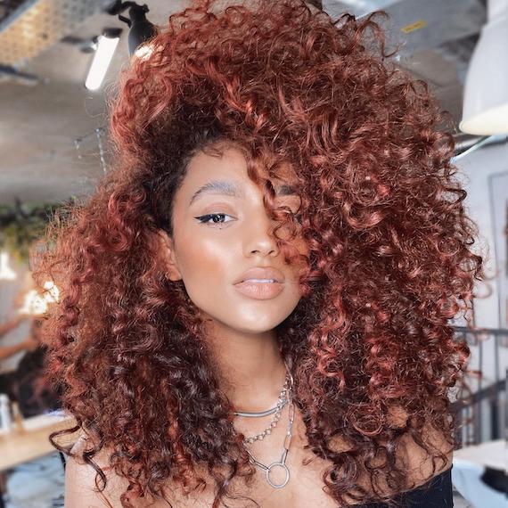 Woman facing the camera with curly, copper red hair, created using Wella Professionals.