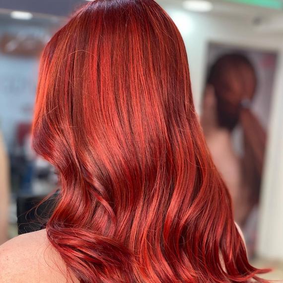 Hinterkopf einer Frau mit langen, locker gewellten, leuchtend roten Haaren, kreiert mit Wella Professionals.