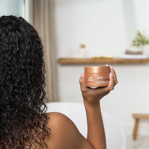 Model with dark brown, curly hair holds up ULTIMATE SMOOTH Mask.