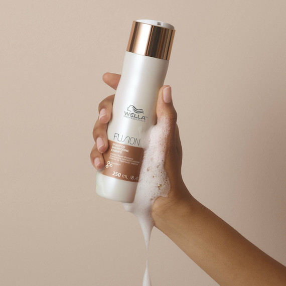 Model’s hand holds up a bottle of Fusion Shampoo.