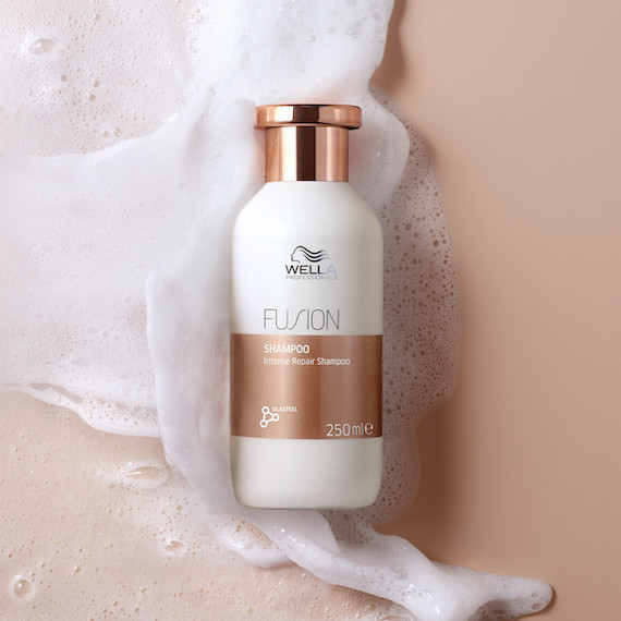 Fusion Shampoo on a blush surface, surrounded by a rich, foamy lather.