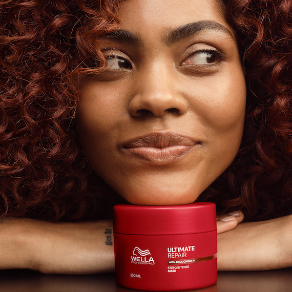 Model with dark brown, curly hair rests chin on tub of ULTIMATE REPAIR Mask.