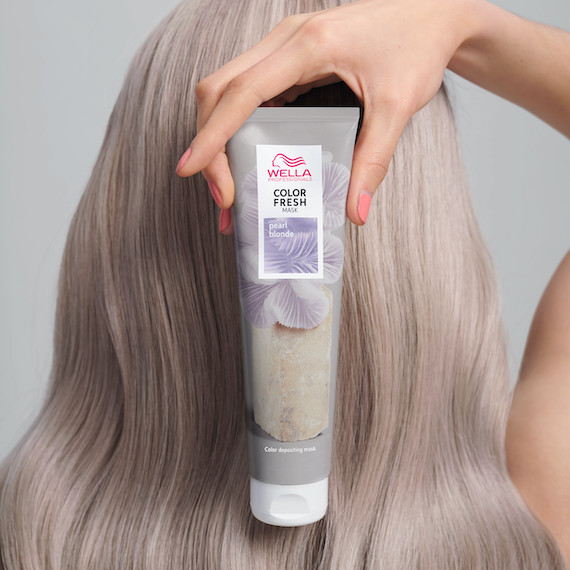 Model with straight, silver blonde hair holds up a tube of Color Fresh Mask in Pearl Blonde.