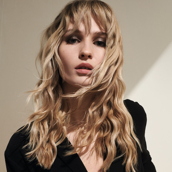 Model with long, wavy blonde hair colored using Koleston Perfect by Wella Professionals looks at the camera