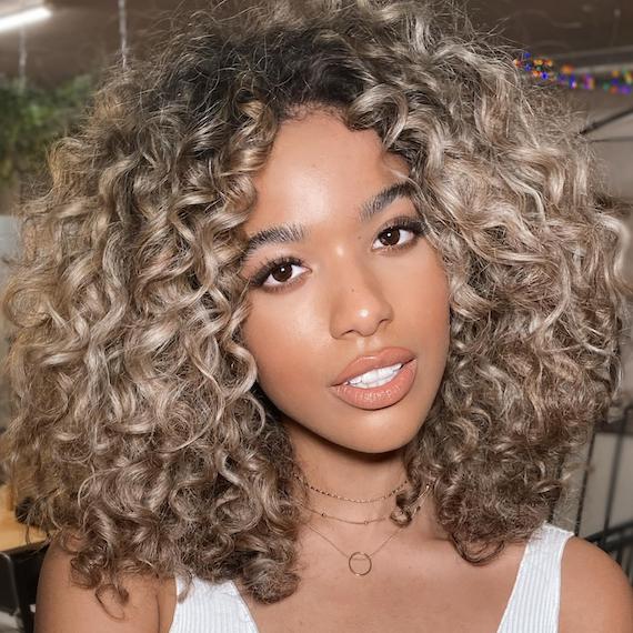 Woman with curly hair and blonde highlights smiles at the camera.