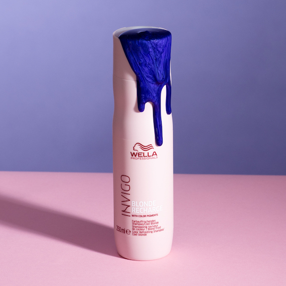 Bottle of INVIGO Cool Blonde Color Refreshing Shampoo on a pink and purple background, with purple liquid coming out of the top.