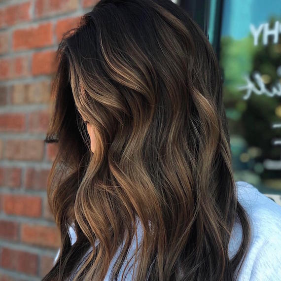 Side profile of woman with partial balayage through long, brown hair, created using Wella Professionals.