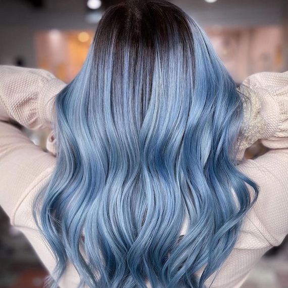 Back of model’s head with long hair featuring brunette roots and pastel blue balayage.