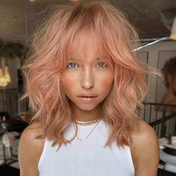 Model with tousled, wavy, pastel hair featuring rose gold, peach and strawberry blonde hues.