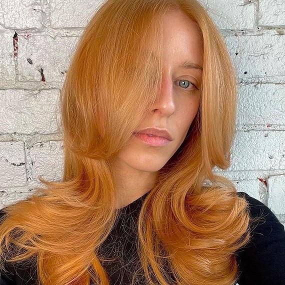 Model with long, blow-dried, strawberry blonde hair with a hint of peach.