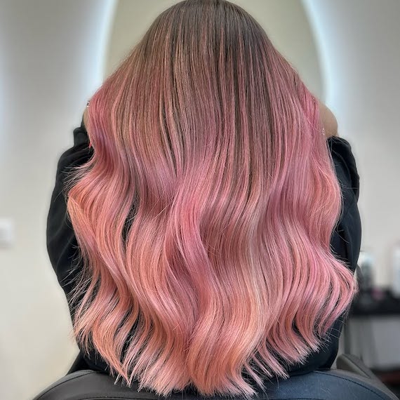 Back of model’s head with long, dark blonde hair featuring a pink balayage.