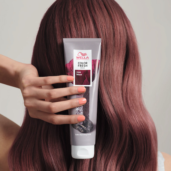 Model with dark pink hair holds up Color Fresh Mask in Rose Blaze.